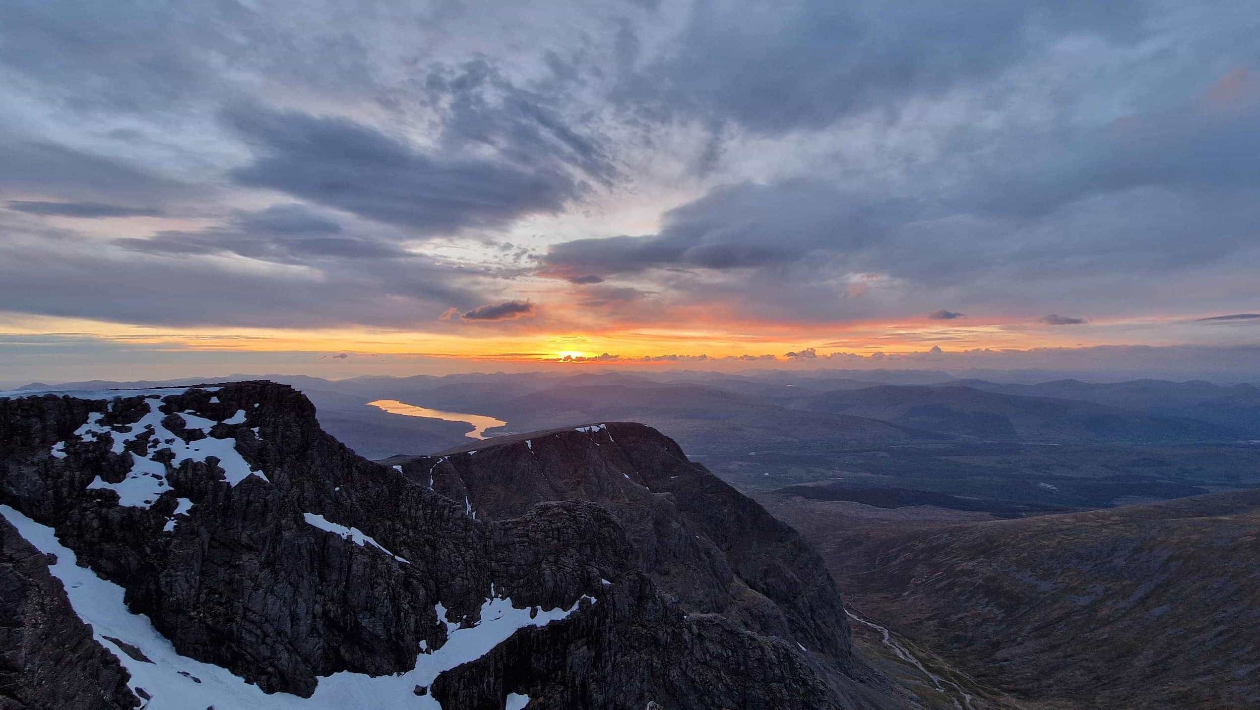 The sun sets behind mountains, casting warm colours over the valley below.